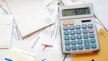 Calculator resting on a pile of various bills and envelopes