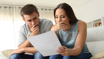Stressed couple sitting on a couch looking at a financial document