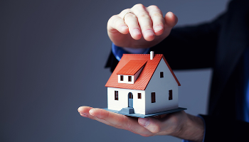 Hands of a person in a suit holding and protecting a model of a small house